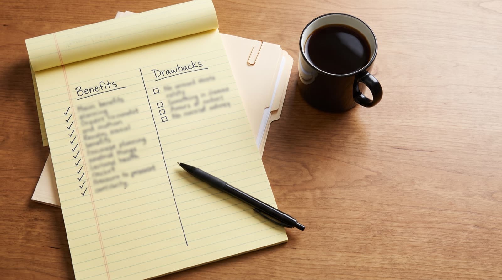 A legal pad on a desk divided into Benefits and Drawbacks columns, with nine checkmarks and four open squares beside a coffee mug